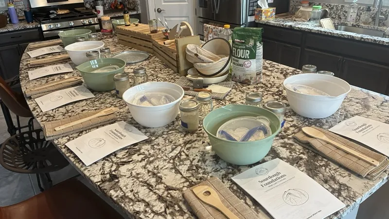 The kitchen island set for Sourdough 101, with a bowl, starter jar, towel, spoon and guide at every seat